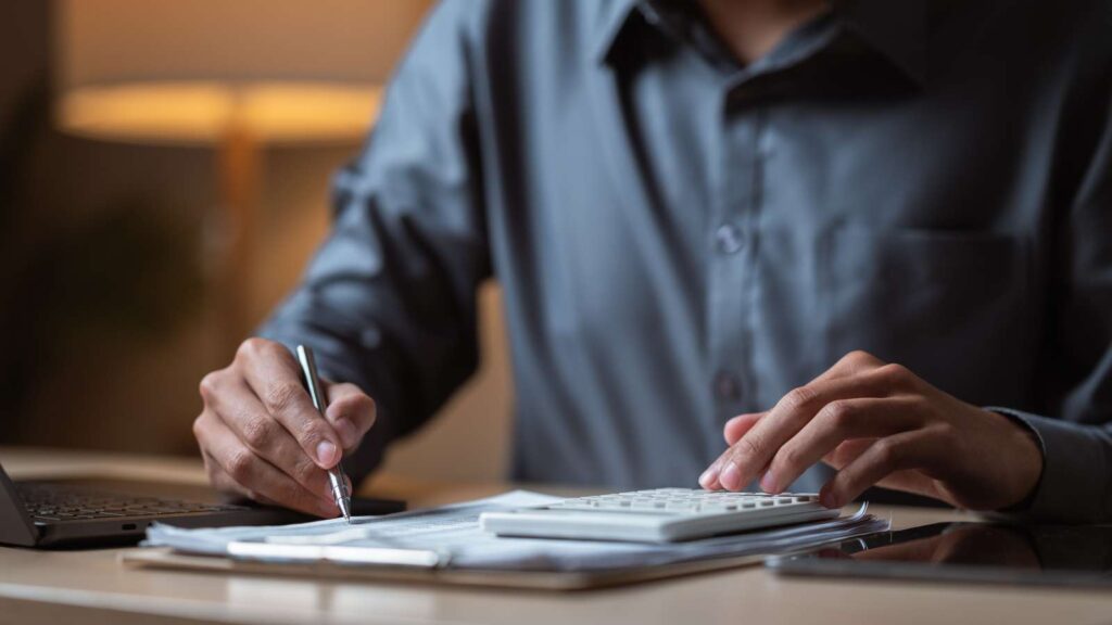 Person calculating office moving costs with a calculator and pen, reviewing budget for a next office relocation.