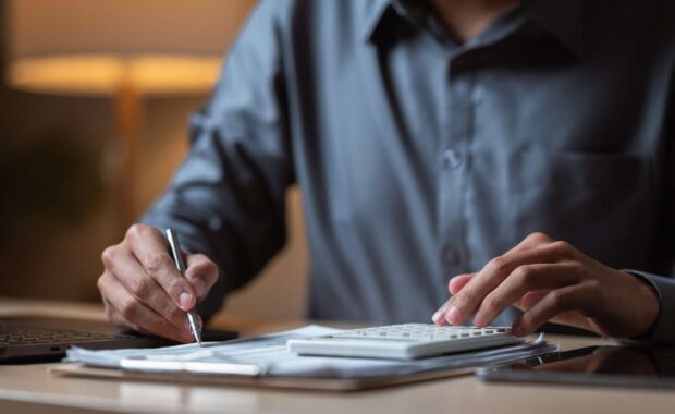 Person calculating office moving costs with a calculator and pen, reviewing budget for a next office relocation.