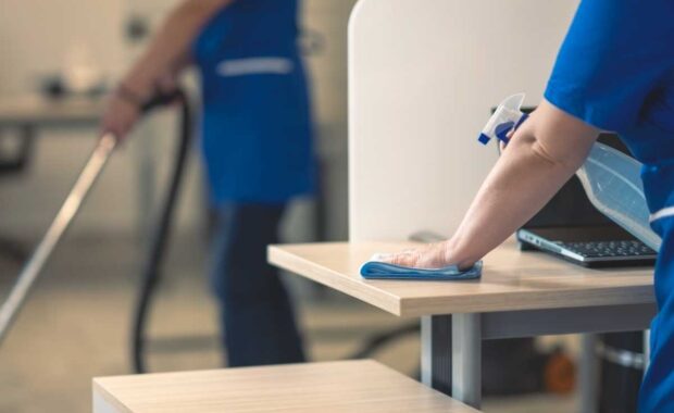 Cleaning an office table.Other cleaners clean in the background