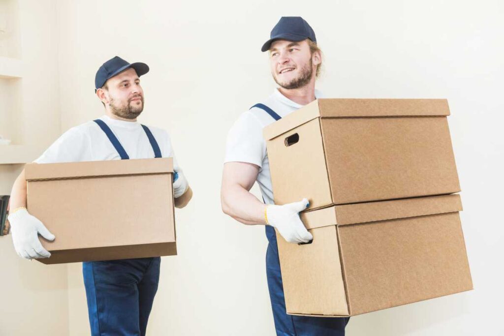 Delivery man loading cardboard boxes for moving to an apartment. professional worker of transportation, male loaders in overalls