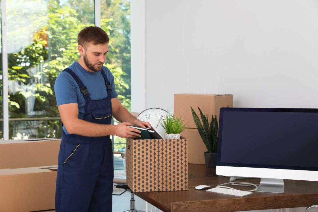Young worker packing stuff into cardboard box at office. Moving service