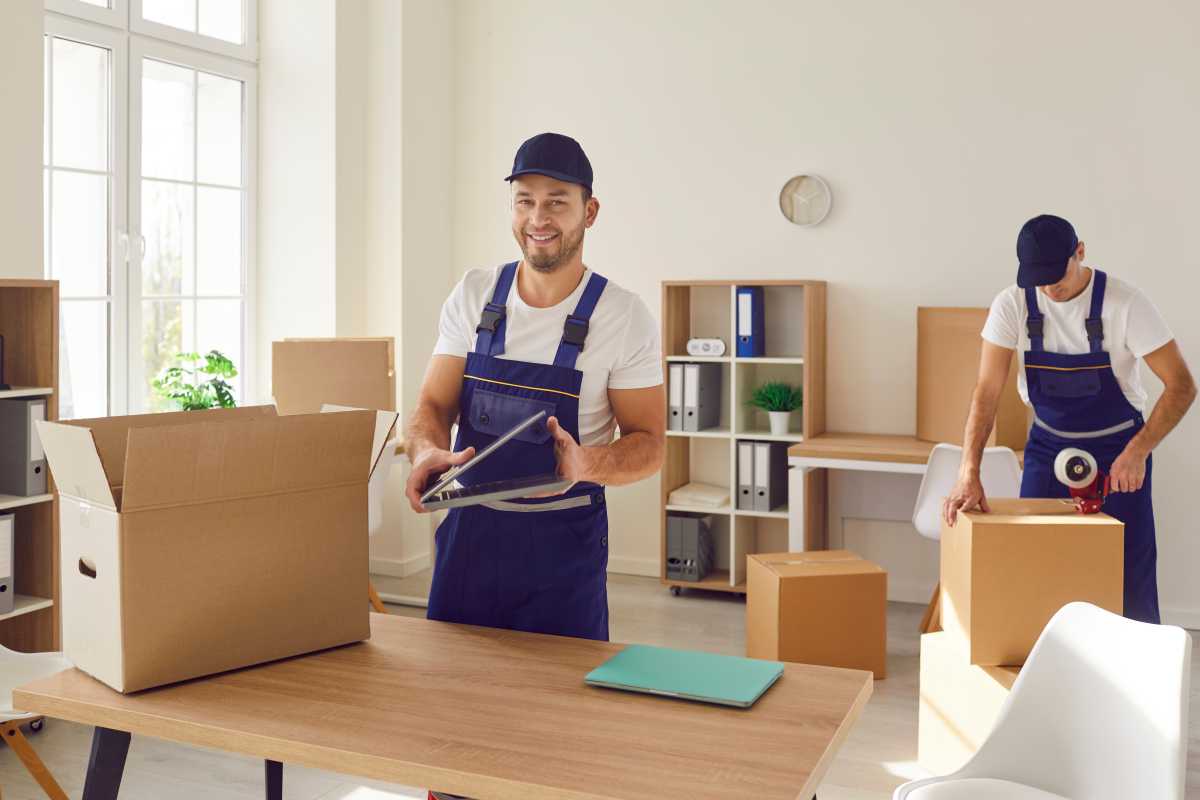 Team of two young male workers from a moving company and removal service packing stuff in cardboard boxes to transport things from one office to another