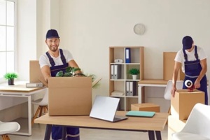 team of young happy cheerful professional workers of moving service in overalls carrying