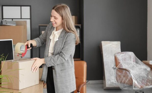 young businesswoman taping box in office on moving day