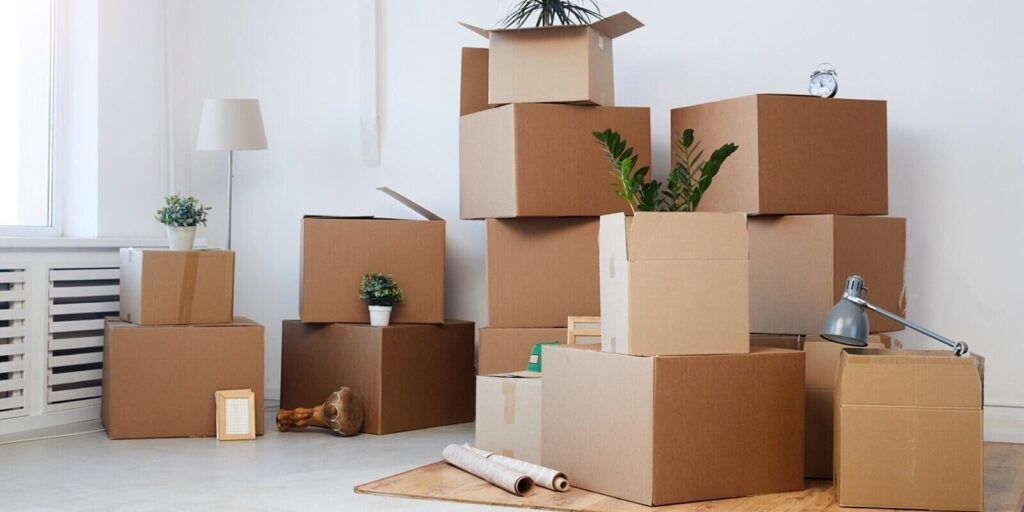 background image of cardboard boxes stacked in empty room with plants and personal belongings inside
