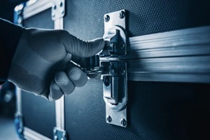 close-up of a gloved hand securing or releasing a metal latch on a rugged, dark professional flight case or road box