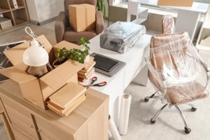 interior of office with desk, boxes and wrapped chairs in stretch film on moving day