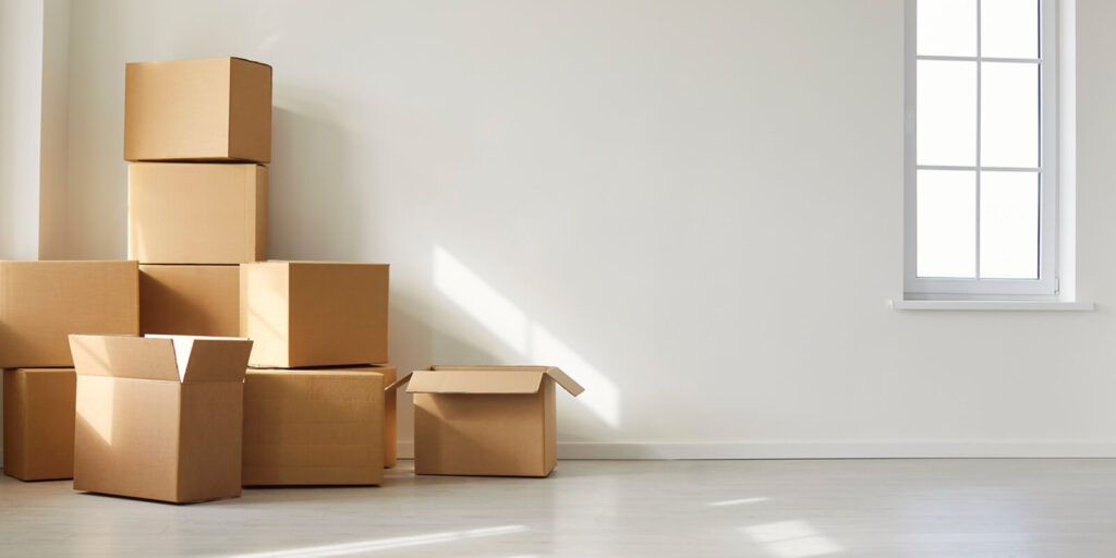 stack of cardboard boxes in empty sunlit room near large window