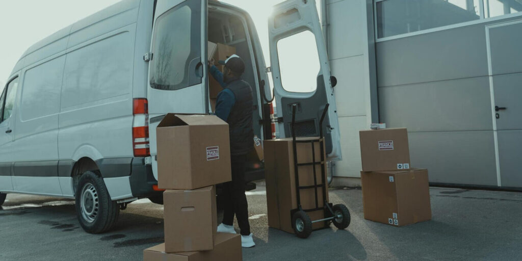 courier loading cardboard boxes into a delivery van outside a warehouse - GSA certified movers