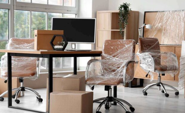interior of modern office with chairs wrapped in stretch film and cardboard boxes on moving day