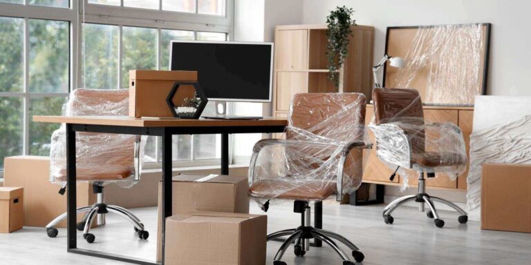 interior of modern office with chairs wrapped in stretch film and cardboard boxes on moving day