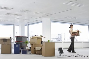 young businesswoman carrying cardboard box near cartons and equipment in empty office space